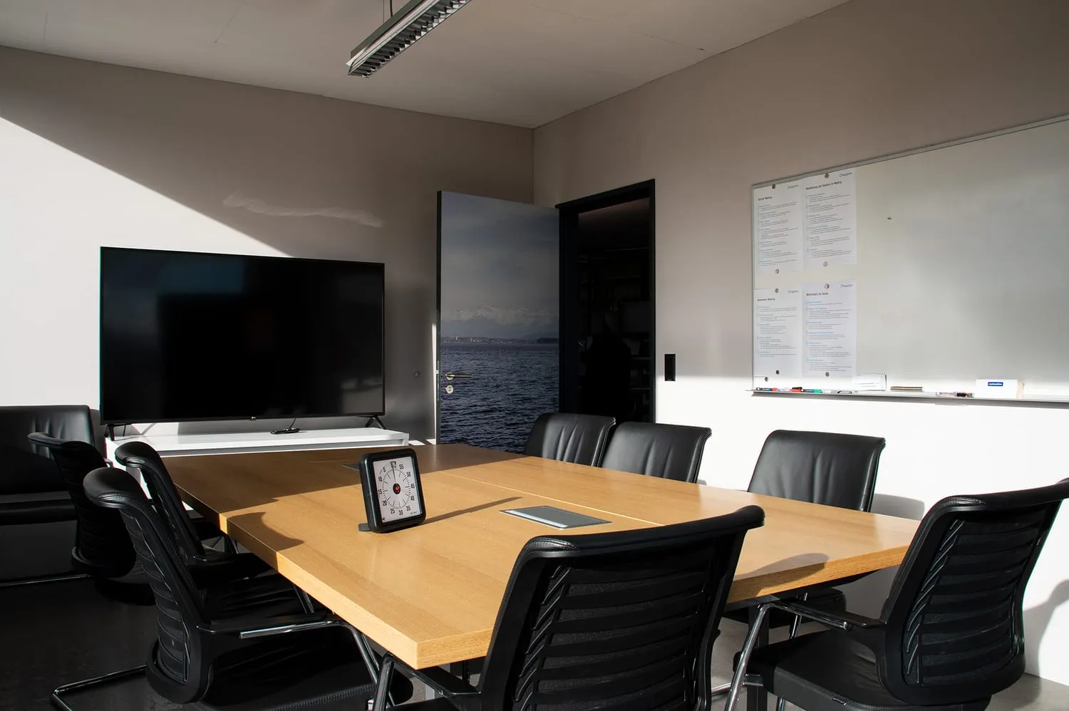 Besprechungsraum mit Holztisch, Bildschirm und Whiteboard, an der Wand die Seetapete