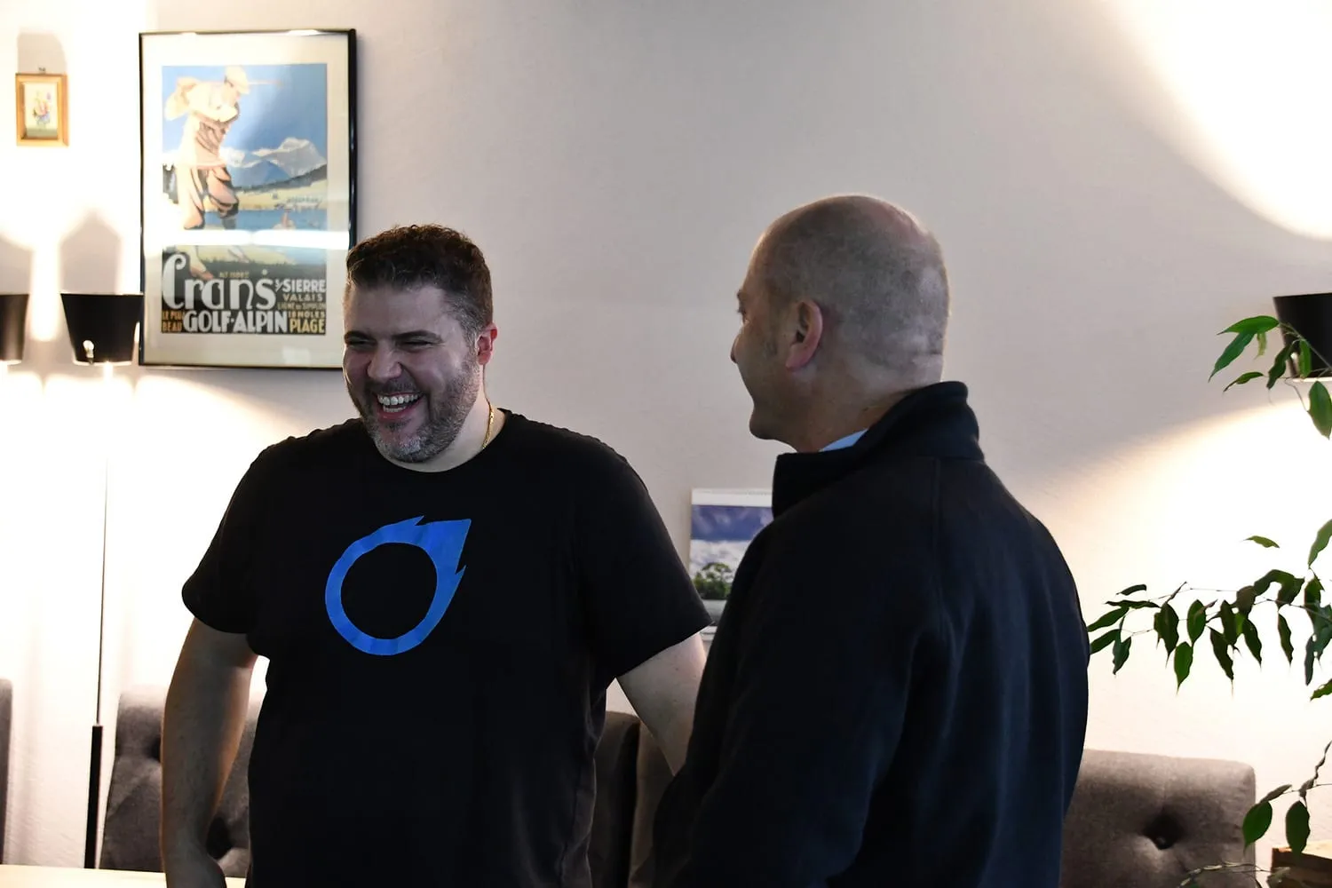 Zwei Gäste lachen im Gespräch, im Hintergrund ein gerahmtes Plakat