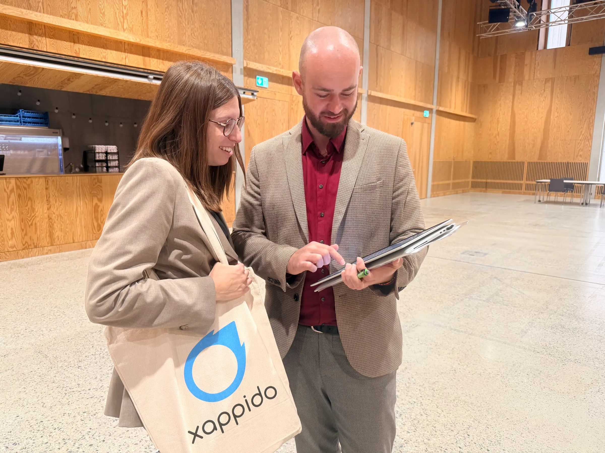 Loredana von xappido mit einer xappido-Tasche und Zsolt Gödri besprechen im Veranstaltungssaal die Einsatzplanung auf dem Tablet